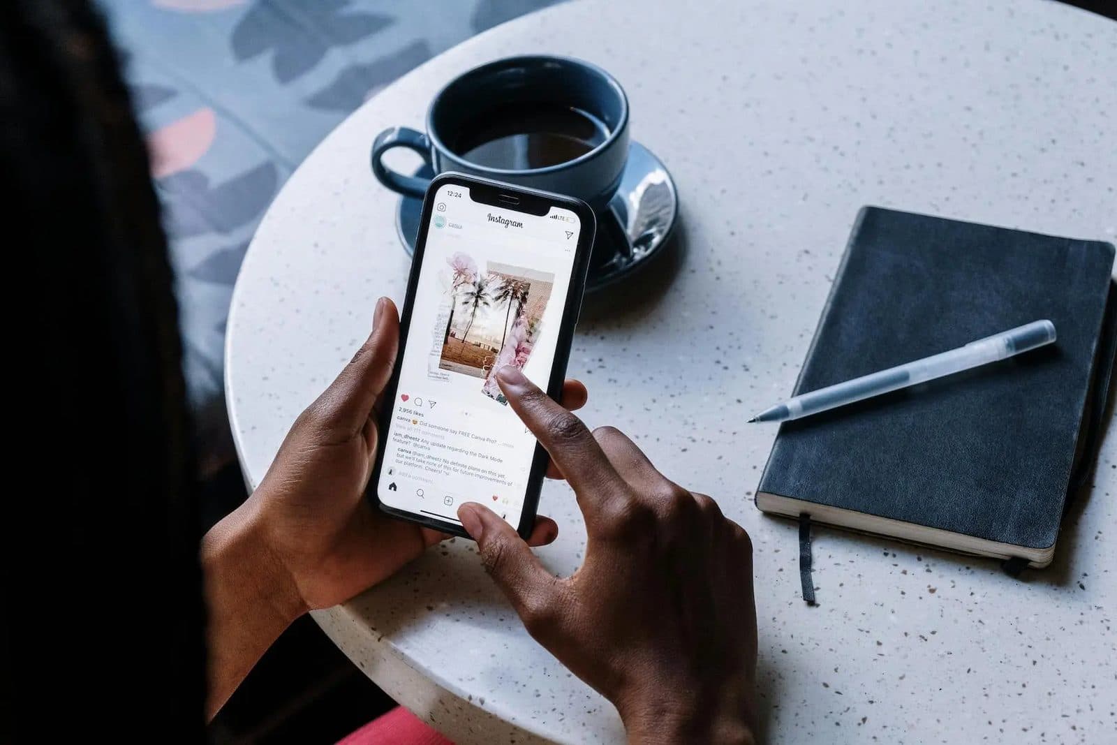 Hand holding a phone showing an Instagram feed next to a coffee and notebook