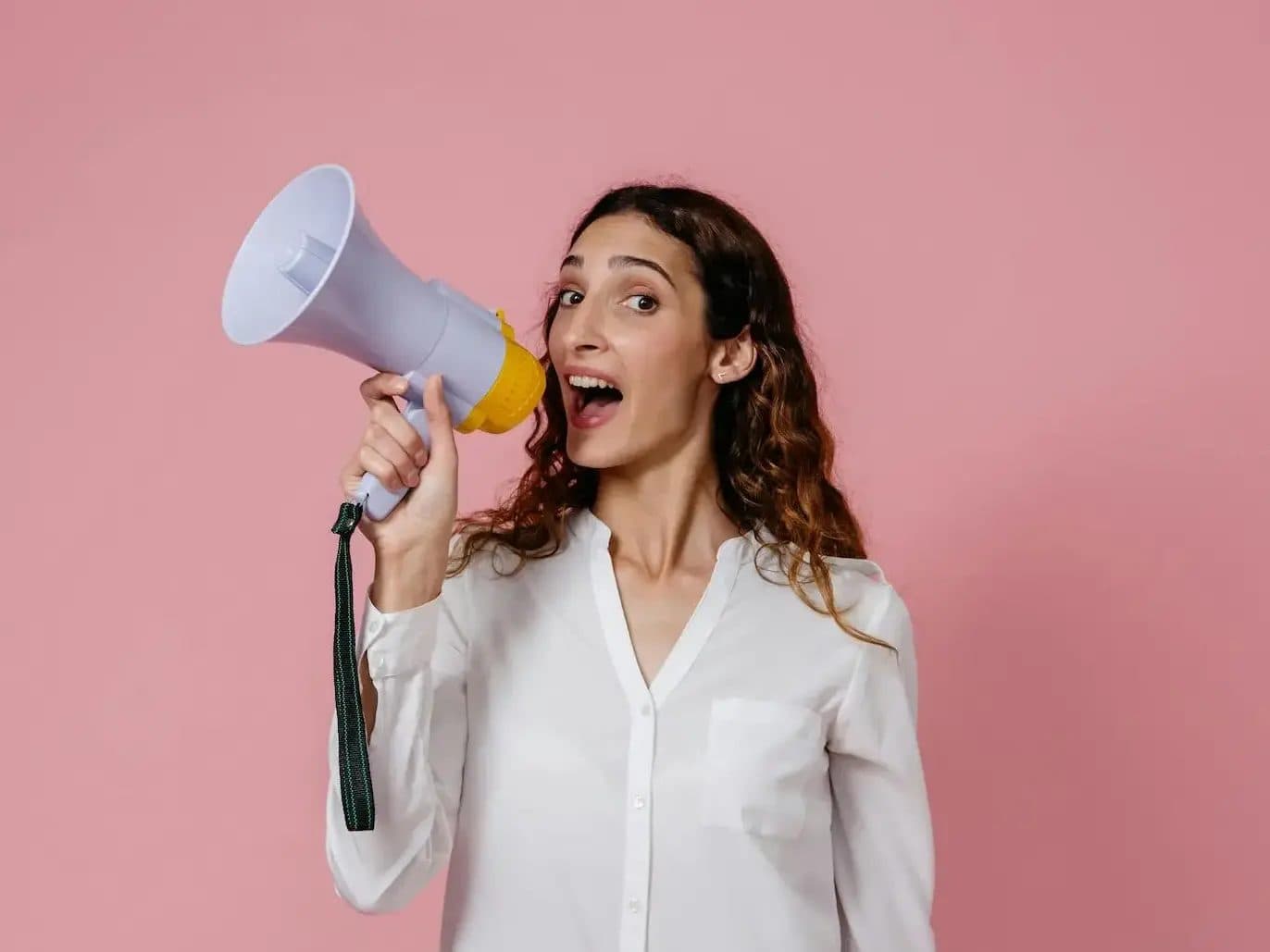 Student shouting into a megaphone against a pink background