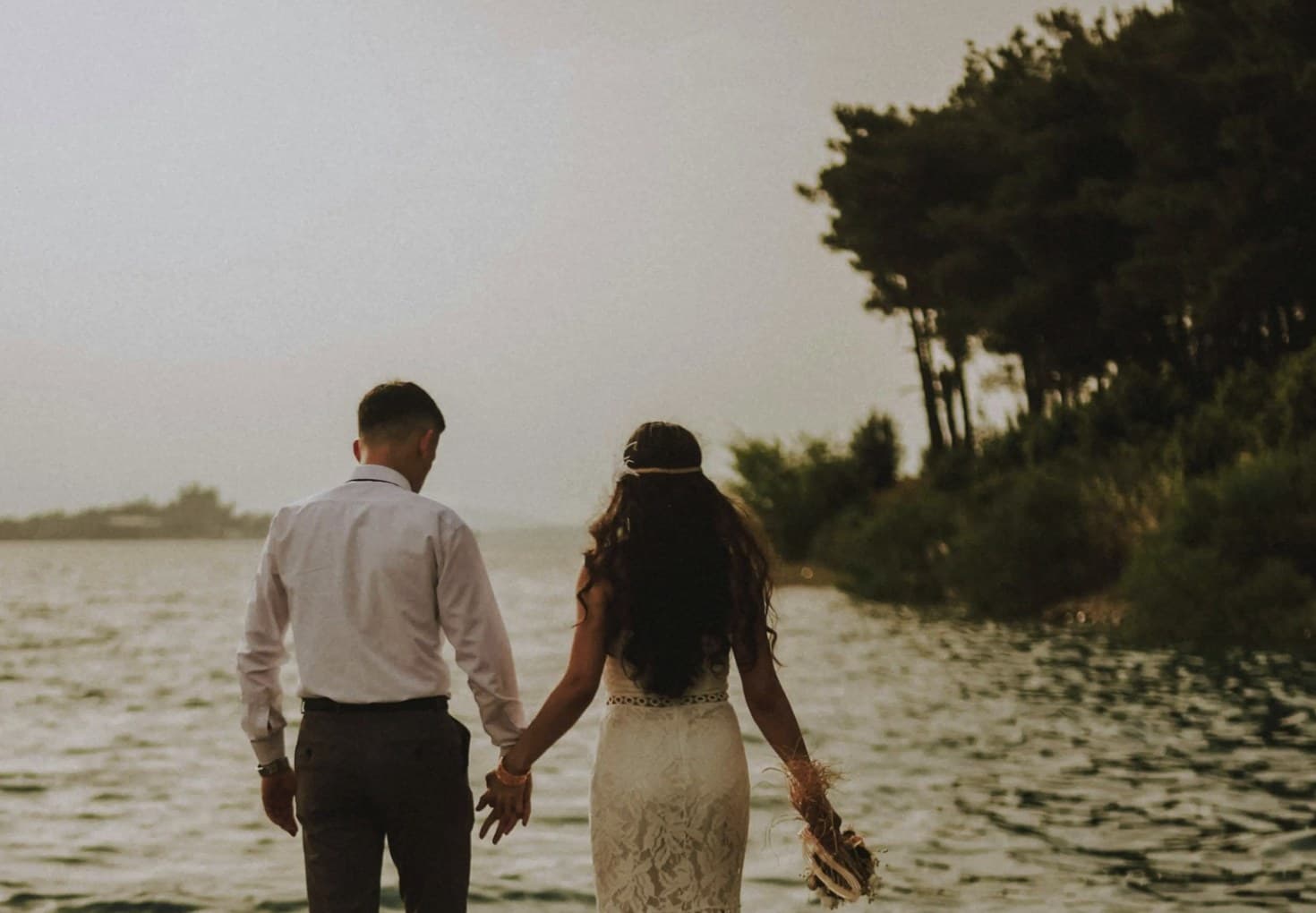 Couple walking hand in hand by the water on their wedding day