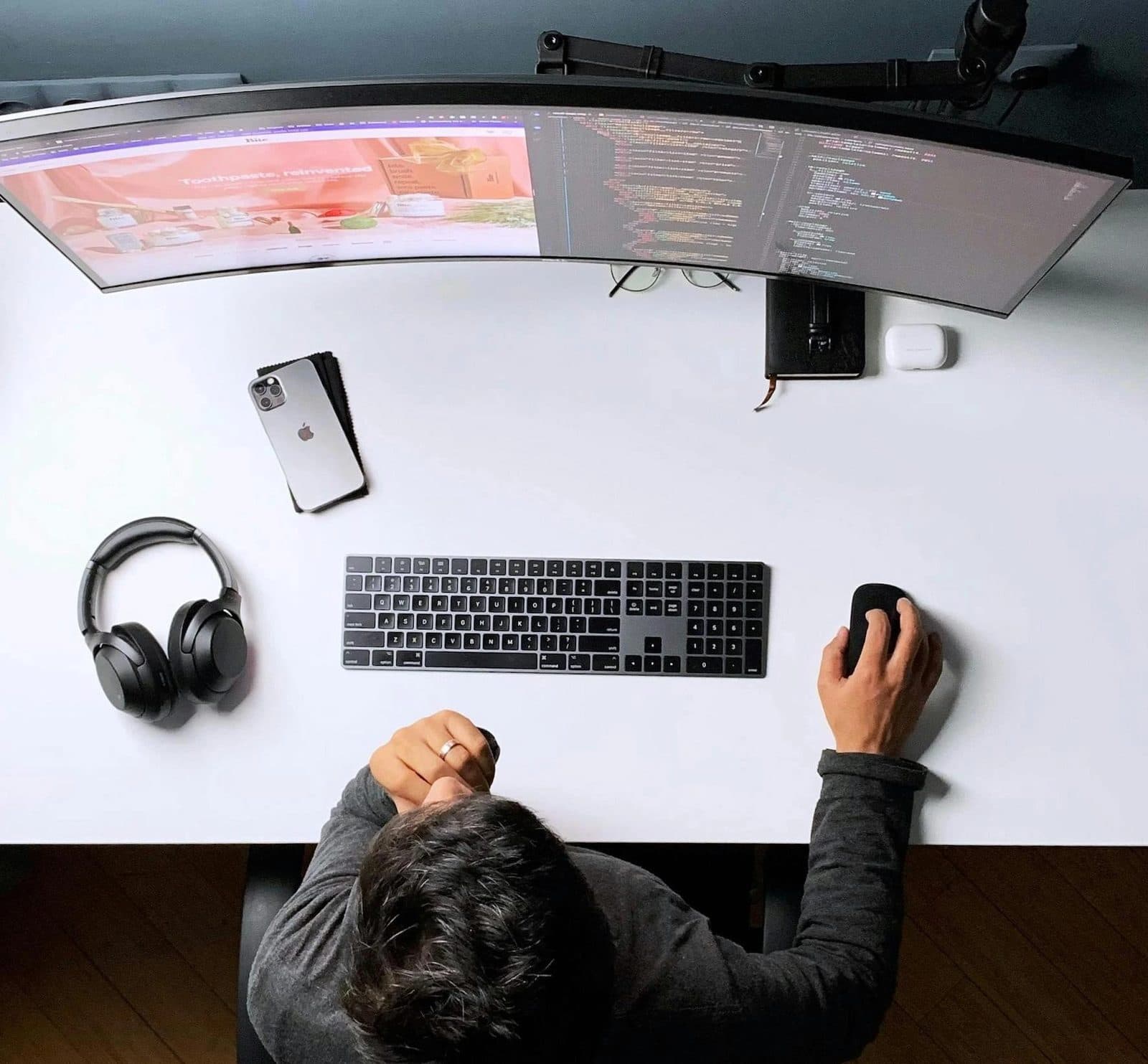 Developer working at a desk with a wide monitor, keyboard and headphones
