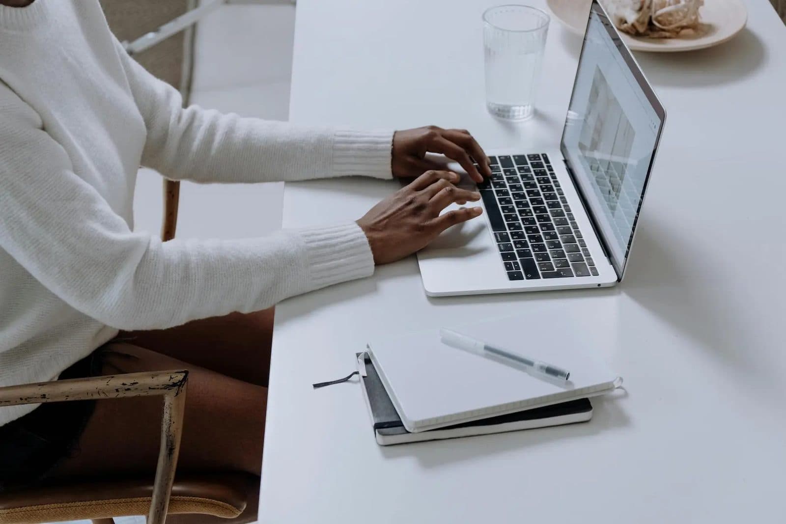 Student typing on a laptop with a notebook and pen beside it